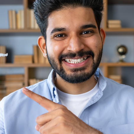 Man smiling at the camera holding a clear aligner retainer and pointing at it.