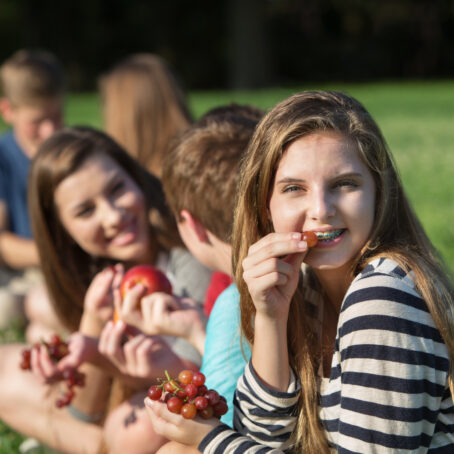 Teenager wearing braces, looking at the camera while eating a grape